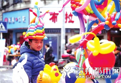 玉屏县城年场上，一个卖气球的人把自己装扮成小丑吸引小孩。 季佩佩 摄